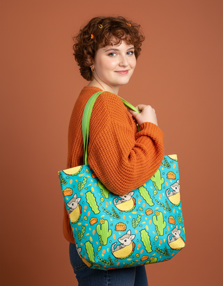 Woman holding a colorful tote bag with cat and cactus design against a brown background