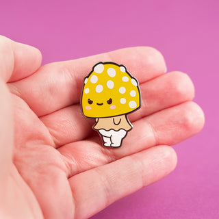 a hand holding a yellow and white mushroom pin